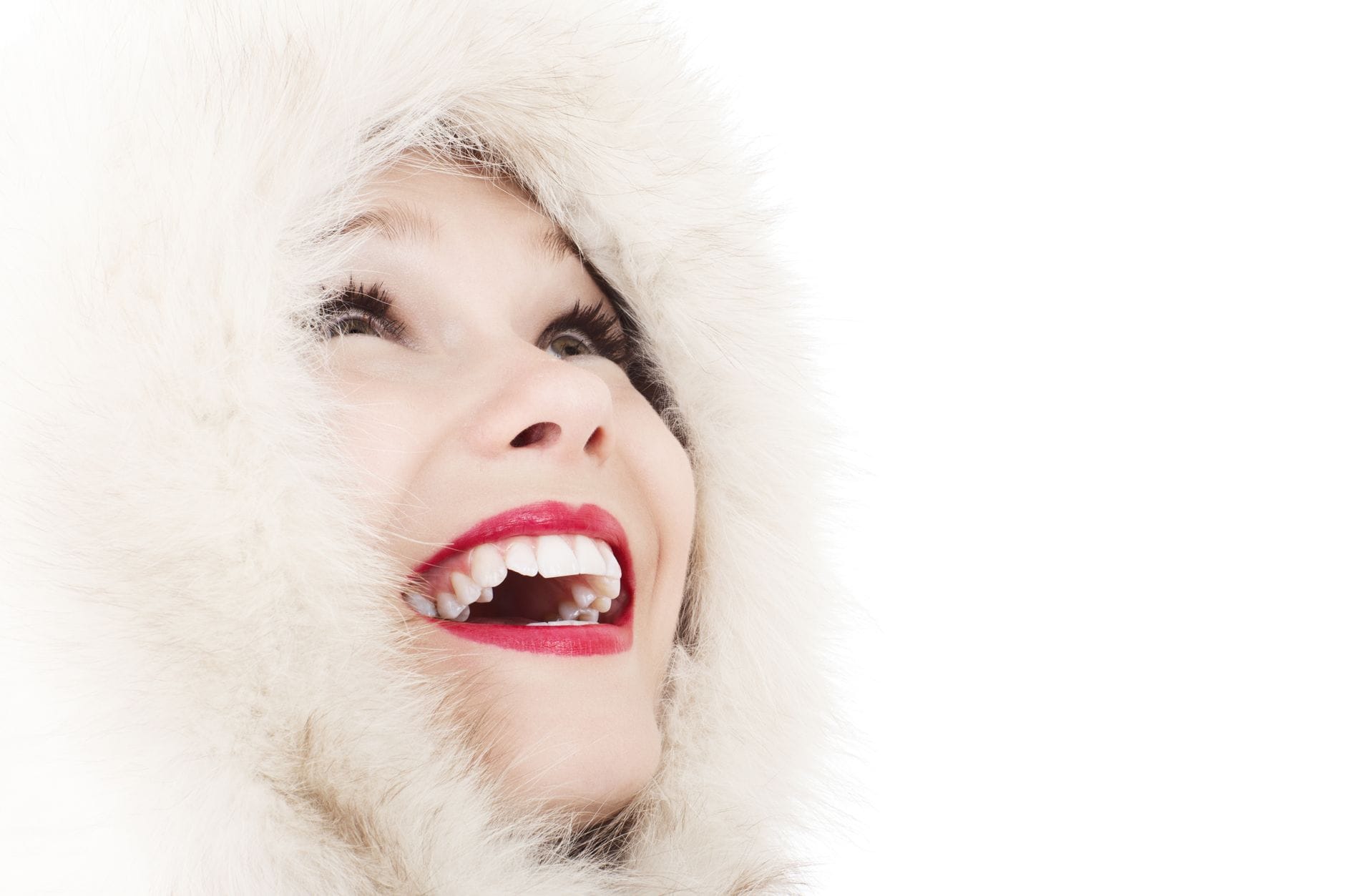 Close-up of a smiling woman in a fluffy white hood, looking upward, with bright red lipstick.