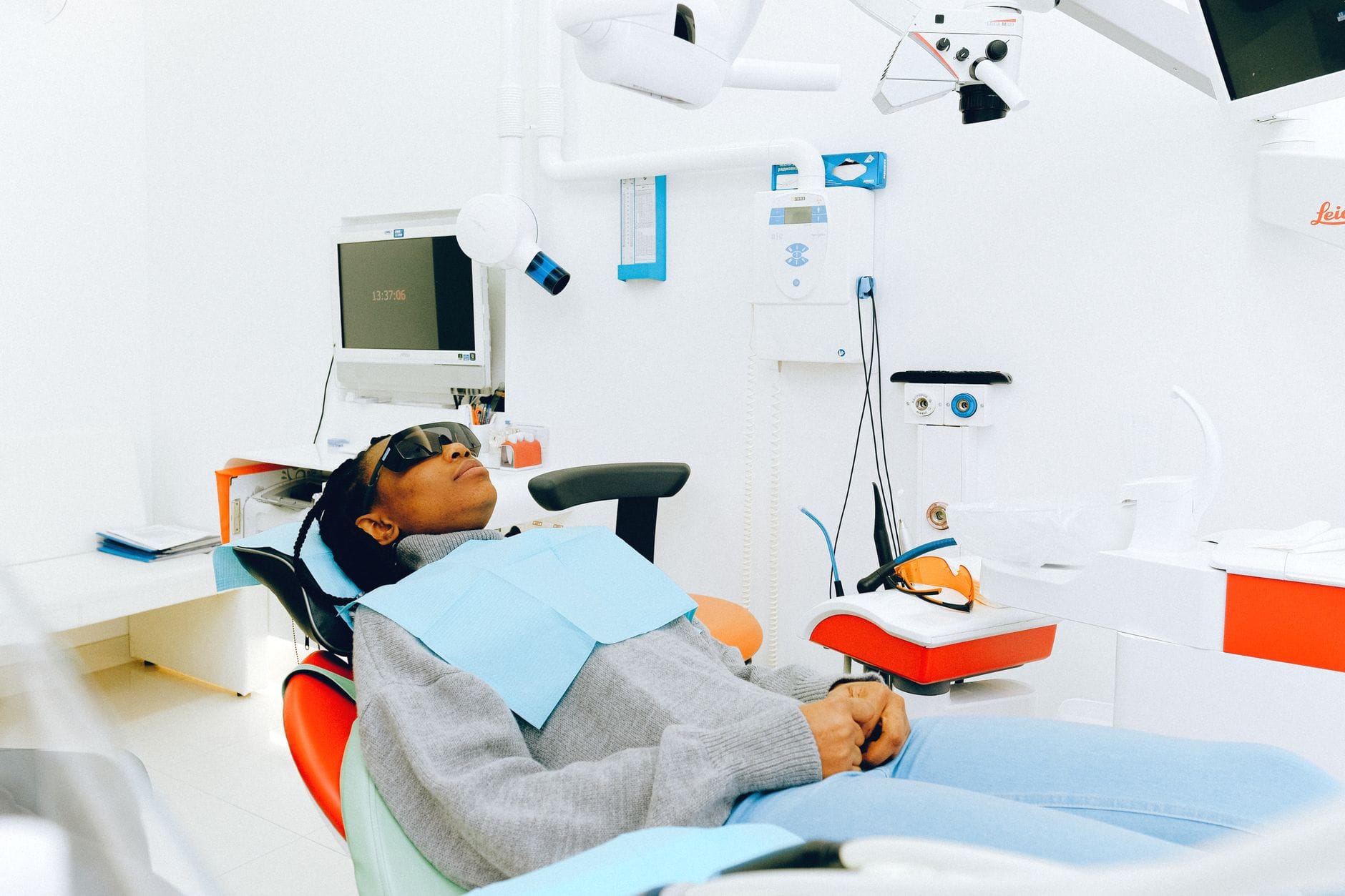 Patient reclining in a dental chair wearing a blue bib in a bright clinic with monitor and equipment nearby