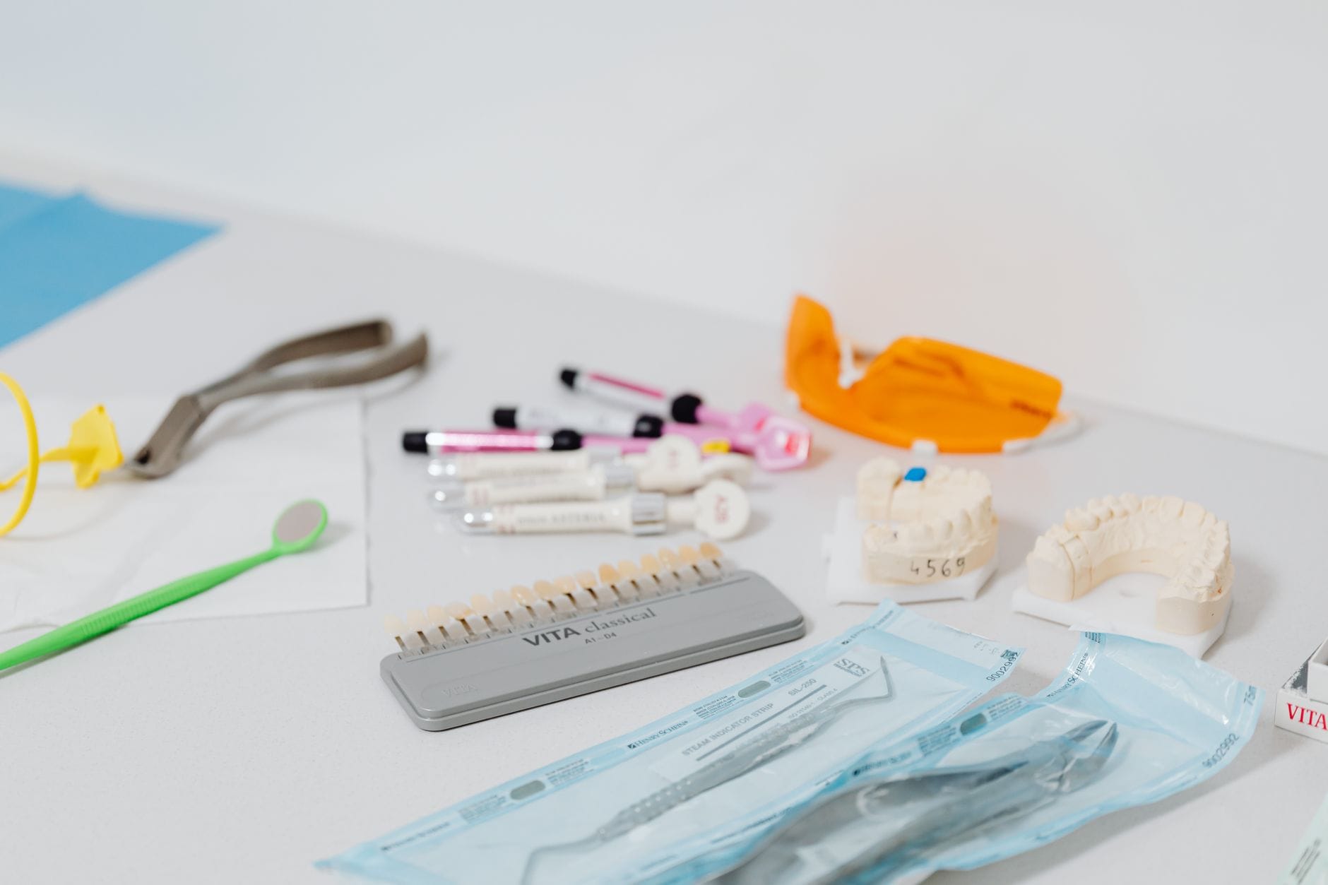 Dental clinic workspace with orthodontic tools, models of teeth, and shade guides laid out on a white table.