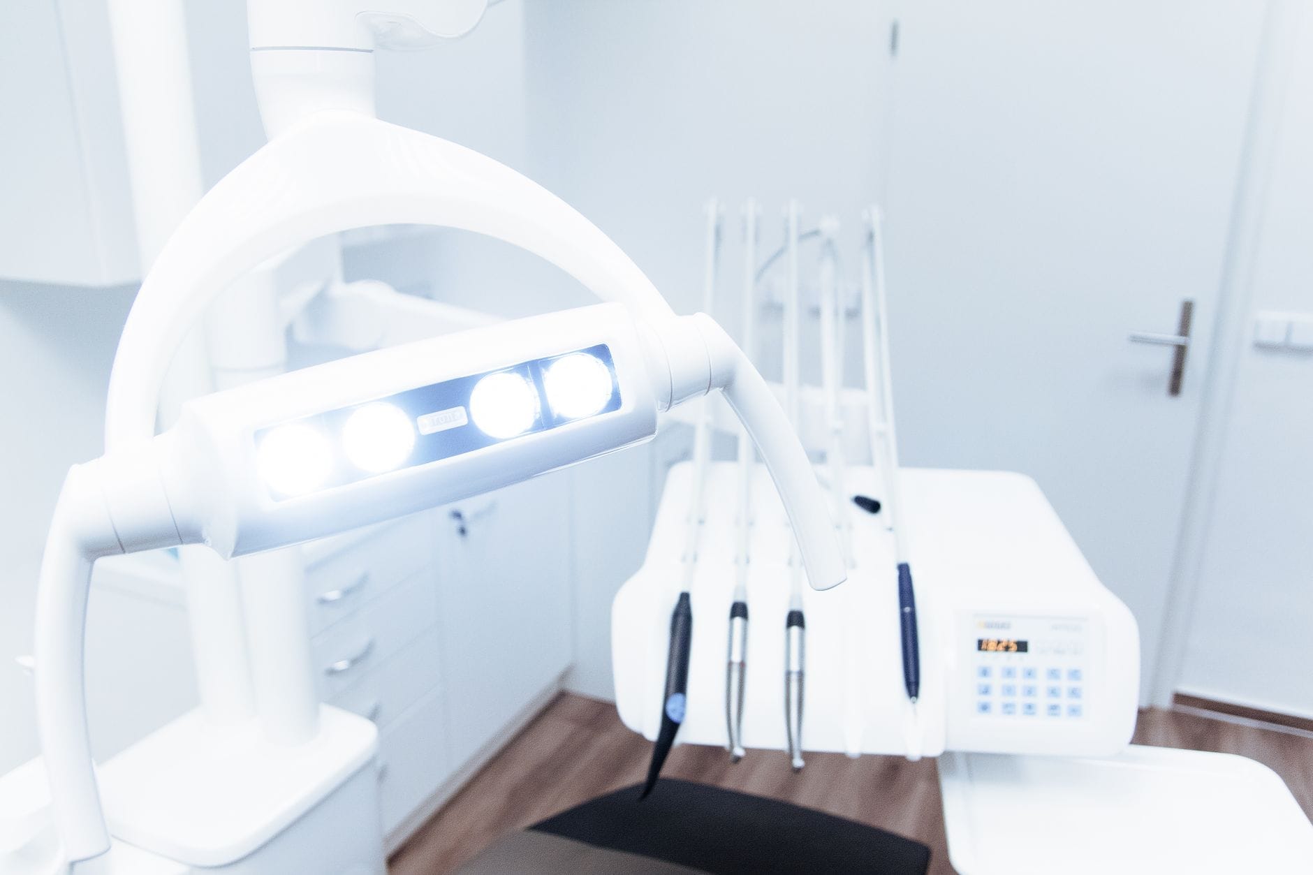 Modern dental chair with overhead light in a clean clinic; dental tools on a tray in the background.