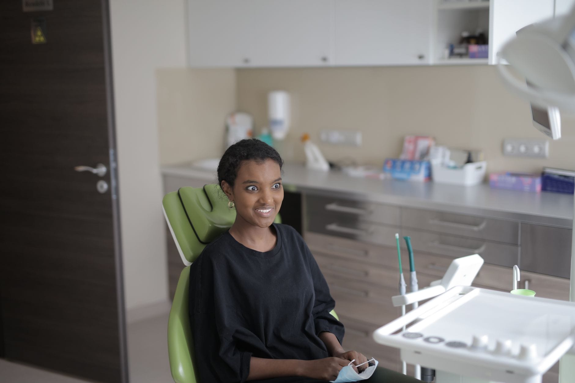 Woman sitting in a dental chair, smiling in a modern clinic with dental equipment nearby.